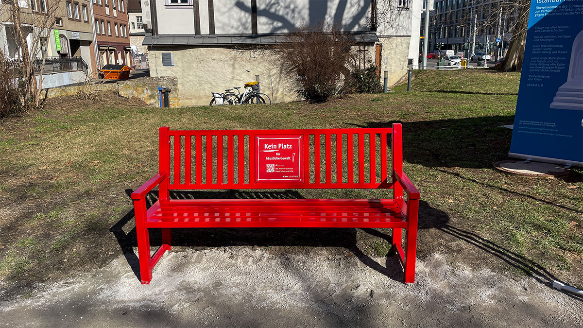 Das Bild zeigt die „rote Bank“, die in Jena am Tag vor dem internationalen Frauentag auf der Freifläche vor dem Platanenhaus der öffentlichkeit vorgestellt wurde. Mit dem Motto Platz nehmen gegen häusliche Gewalt.